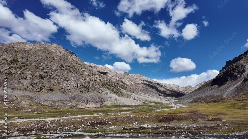 4K Mountain Landscape Side View of a Flowing River Through Grassy Meadows Leading to Rocky Mountain Ranges,Cinematic Scene Featuring Fluffy Clouds in a Blue Sky,Lighting Highlighting Sunlit,Dark,Peaks 4K Mountain Landscape Side View of a Flowing River Through Grassy Meadows Leading to Rocky Mountain Ranges,Cinematic Scene Featuring Fluffy Clouds in a Blue Sky,Lighting Highlighting Sunlit,Dark,Peaks