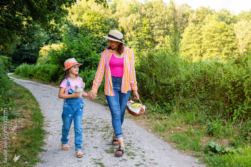 Fototapeta premium Mother and her daughter are walking together in a forest park. Woman and a girl are going on a family picnic.