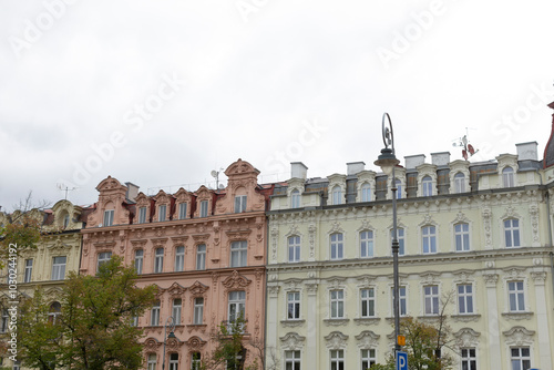 A row of interesting buildings, each adorned with trees in front of them, stands majestically under a cloudy day sky filled with gray clouds