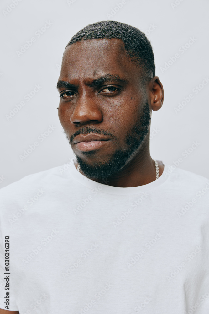 Portrait of a confident black man with a serious expression, wearing a white t shirt, set against a soft gray background, conveying strength and individuality Portrait of a confident black man with a serious expression, wearing a white t shirt, set against a soft gray background, conveying strength and individuality