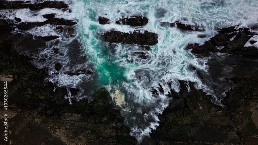 The ocean waves crash against the black rocks, creating white foam that contrasts with the dark green seawater. The water flow appears strong, breaking through the rough rock crevices. The ocean waves crash against the black rocks, creating white foam that contrasts with the dark green seawater. The water flow appears strong, breaking through the rough rock crevices.