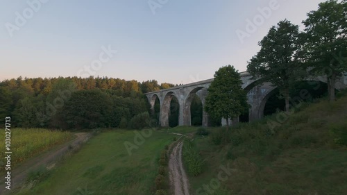 Aerial view of the historic Stanczyki Bridge amidst lush greenery and fields under the evening sky in Poland. High quality 4k footage photo