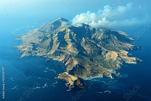 This aerial perspective showcases a rugged volcanic island surrounded by stunning blue waters, with wisps of smoke rising from the terrain suggesting volcanic activity