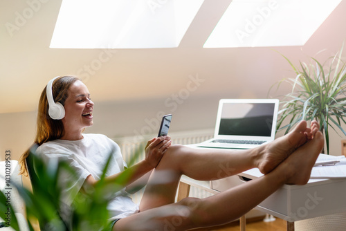 Young brunette woman sitting with feet up on the table using her cellphone and laughing. photo