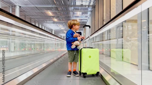 Child boy with teddy bear and suitcase at airport on travelator