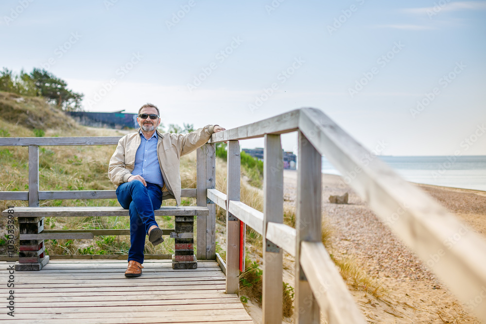 Older man in sunglasses sitting on a bench on a boardwalk by the beach Older man in sunglasses sitting on a bench on a boardwalk by the beach