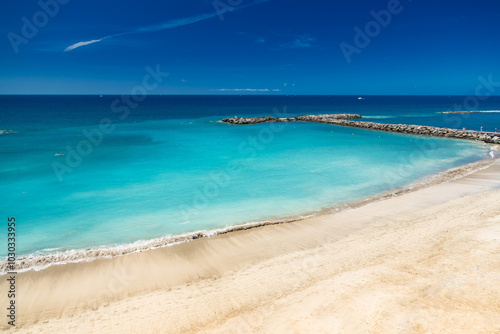 Beautiful Playa del Duque’s turquoise waters and golden shoreline sparkle under the clear blue sky on a sunny day