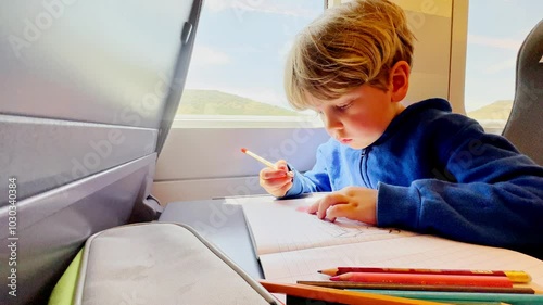 Young boy drawing attentively on a train ride, pencil lay aside