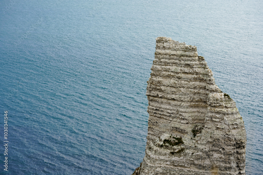 A tall, jagged rock formation rises out of the sea with calm waters in the background A tall, jagged rock formation rises out of the sea with calm waters in the background