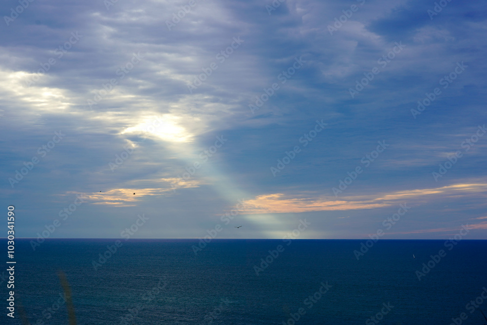 Fototapeta premium The vast ocean meets the horizon under a dramatic sky pierced by a ray of light