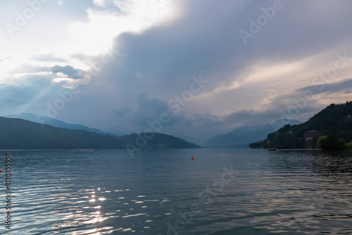 Scenic view of Lake Millstatt surrounded by majestic mountain range bathed in soft light of dusk in Carinthia, Austria. Idyllic lakeshore with remote villages. Wanderlust Austrian Alps. Misty ridges photo