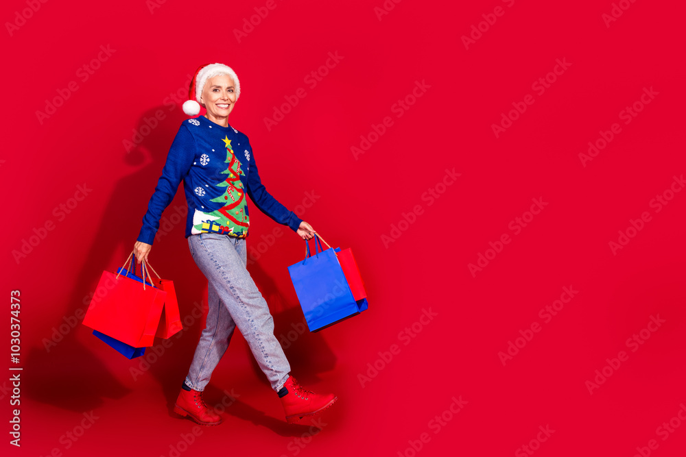 Full body portrait of pretty aged lady hold bags walk empty space new year xmas isolated on vibrant red color background Full body portrait of pretty aged lady hold bags walk empty space new year xmas isolated on vibrant red color background
