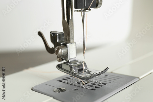 Sewing machine with beige thread on light background, closeup