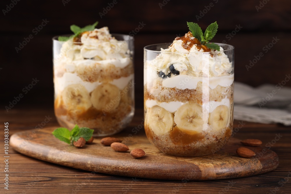 Tasty trifle dessert. Sponge cake, banana and whipped cream in glasses on wooden table, closeup Tasty trifle dessert. Sponge cake, banana and whipped cream in glasses on wooden table, closeup