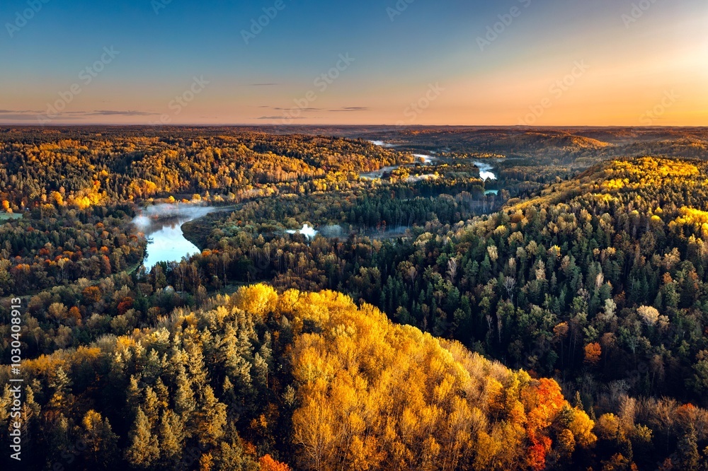 Colorful sunrise over the Gauja National park valley. Sigulda city panorama from drone with forest in autumn colors.