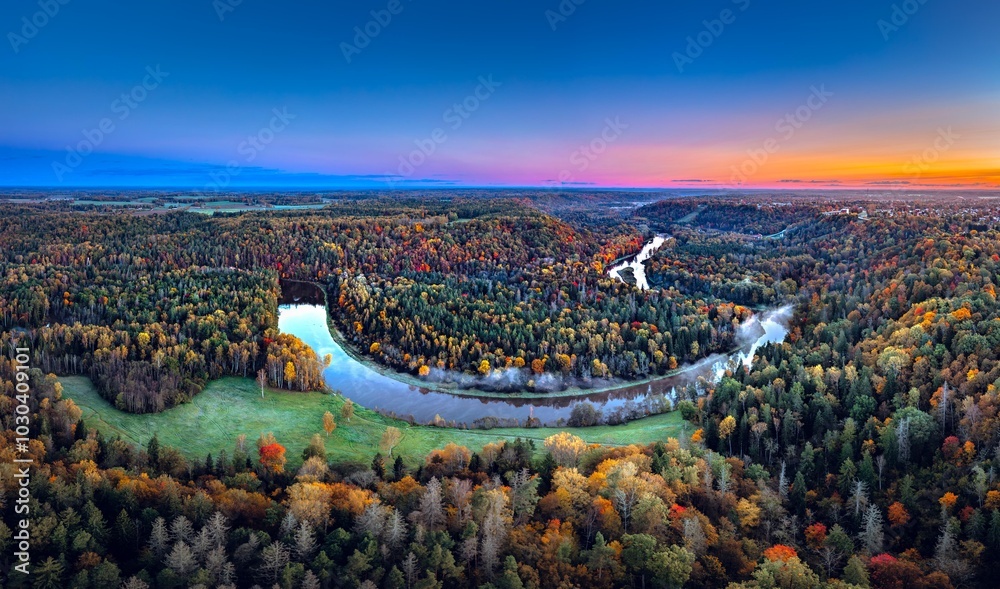 Colorful sunrise over the Gauja National park valley. Sigulda city panorama from drone with forest in autumn colors.