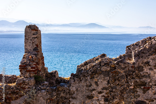 The ancient wall of fortress on to of huge basalt rock over the sea. Blue water  devide the picture into two parts with sea water and the secont with abandoned  and destroyed fortress on cliff
 photo