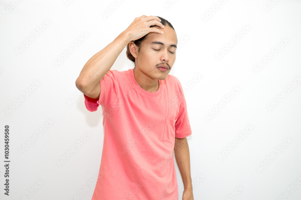 An Indonesian, Asian man wearing a pink tshirt having a headache, chest pain and stomach ache with hands holding head, chest and stomach. isolated in white background An Indonesian, Asian man wearing a pink tshirt having a headache, chest pain and stomach ache with hands holding head, chest and stomach. isolated in white background
