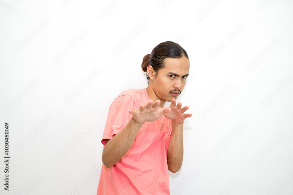 An Indonesian, Asian man wearing a pink tshirt shows a fierce expression as if he is angry or frustrated. isolated in white background An Indonesian, Asian man wearing a pink tshirt shows a fierce expression as if he is angry or frustrated. isolated in white background