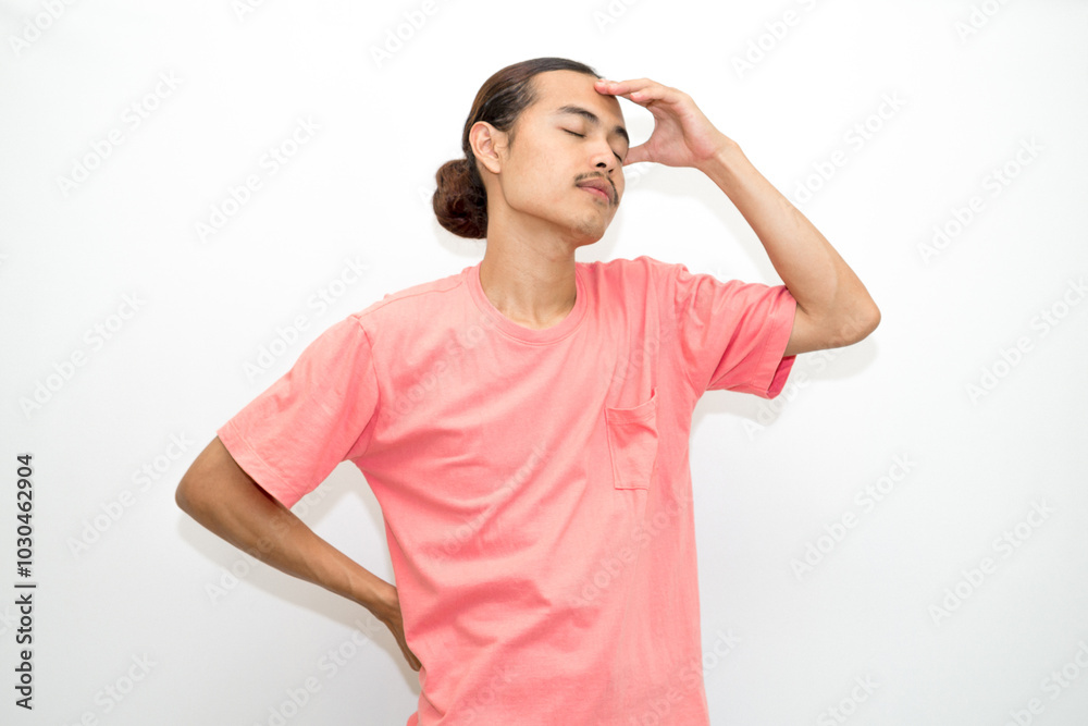An Indonesian, Asian man wearing a pink tshirt having a headache, chest pain and stomach ache with hands holding head, chest and stomach. isolated in white background An Indonesian, Asian man wearing a pink tshirt having a headache, chest pain and stomach ache with hands holding head, chest and stomach. isolated in white background