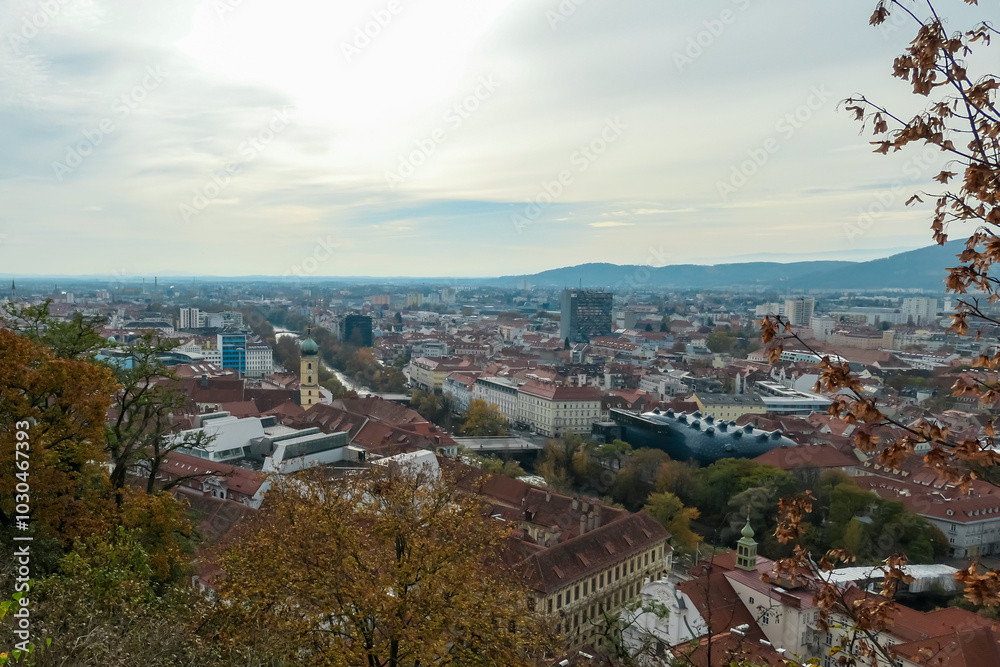 Naklejka premium Scenic aerial view of Graz seen from Schlossberg, Styria, Austria, Europe. Unesco world heritage site with red-roofed buildings. City is nestled amidst rolling hills. Overcast cloudy day