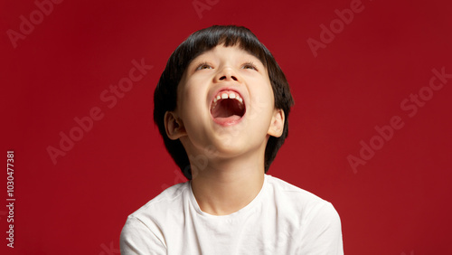 фотографія Child, Asian boy laughs with his head thrown back, mouth wide open, fully immersed in moment against bold red studio background