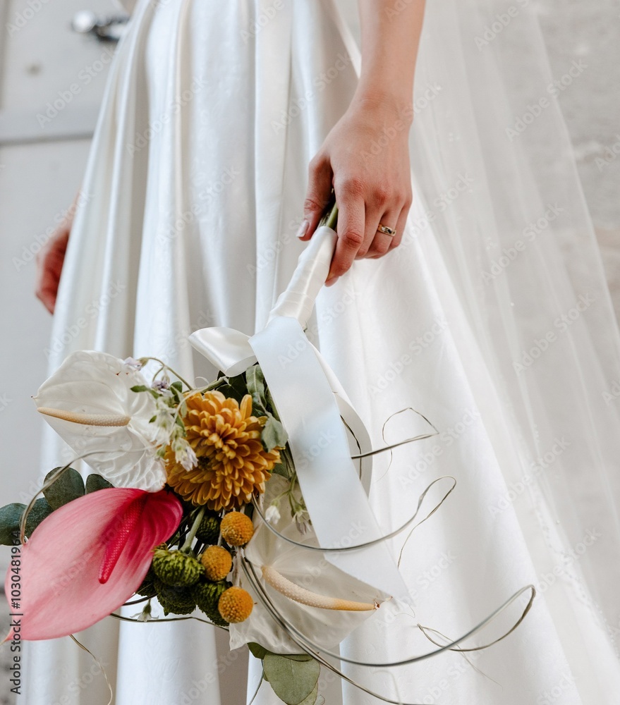 Elegant bridal bouquet with tropical flowers and modern ribbon details held by a bride in a wedding dress.