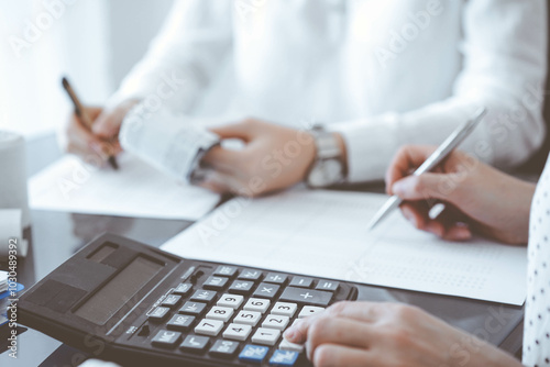 Two accountants use a calculator and laptop computer for counting taxes or revenue balance. Business, audit, and taxes concepts photo