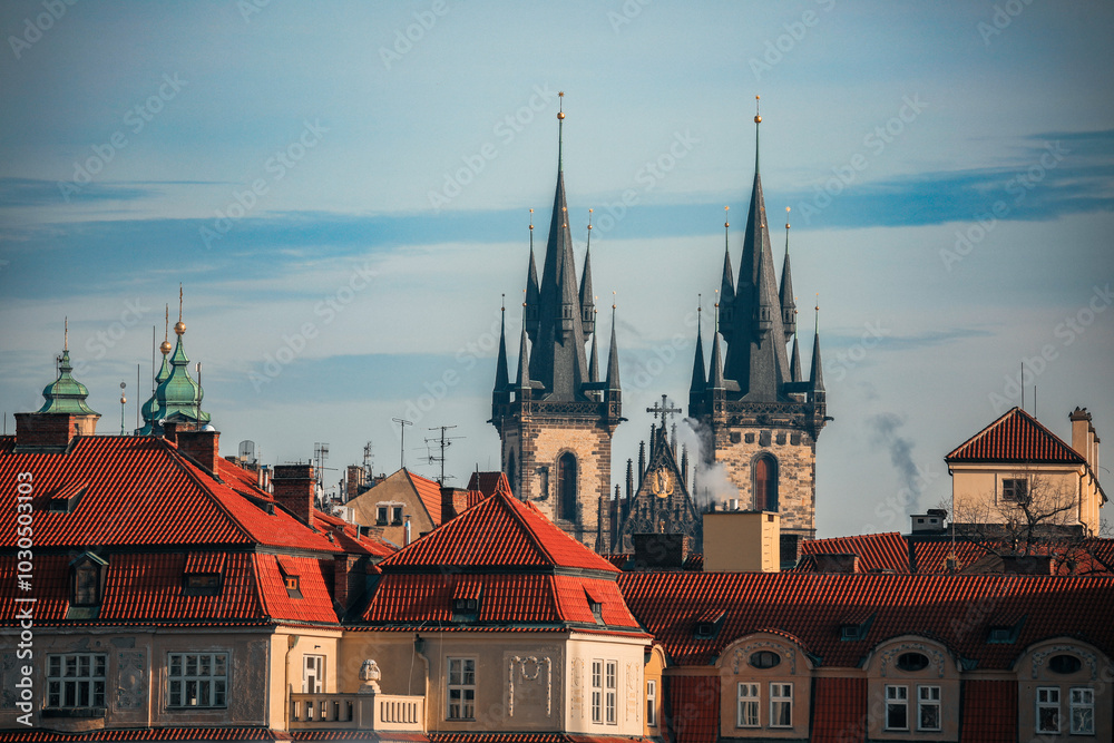 Gothic spires of Prague rise above red rooftops on a clear day, showcasing the city's historic architecture and charm Gothic spires of Prague rise above red rooftops on a clear day, showcasing the city's historic architecture and charm