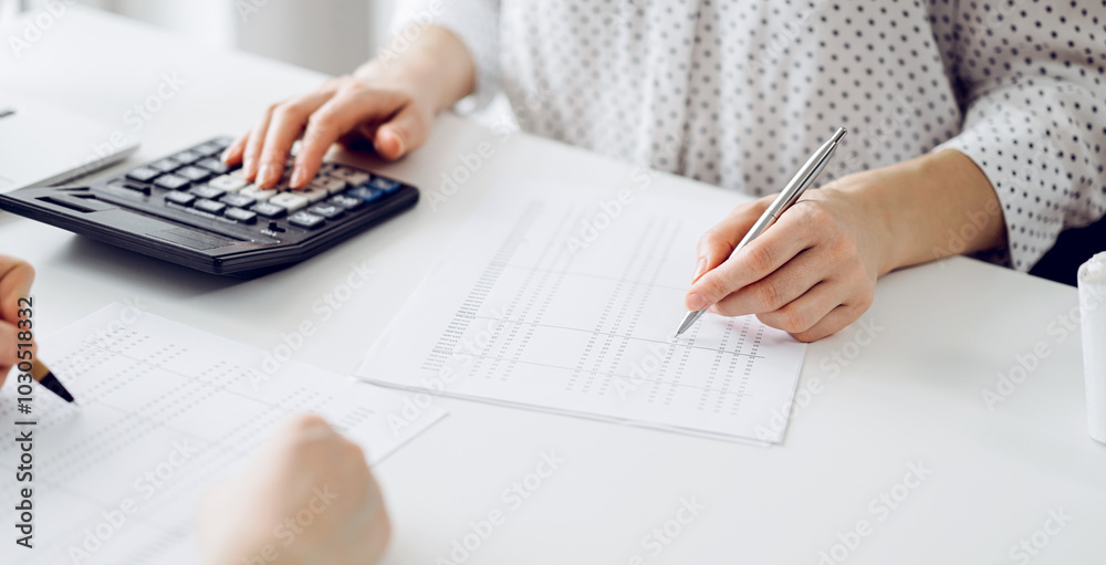 Two accountants using a calculator and laptop computer for counting taxes at white desk in office. Teamwork in business audit and finance Two accountants using a calculator and laptop computer for counting taxes at white desk in office. Teamwork in business audit and finance