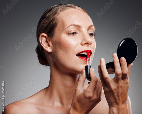 Woman, mirror and apply lipstick in studio, red color and beauty cosmetics on gray background. Female person, skincare and tool for makeup treatment or product, dermatology and compact for grooming
