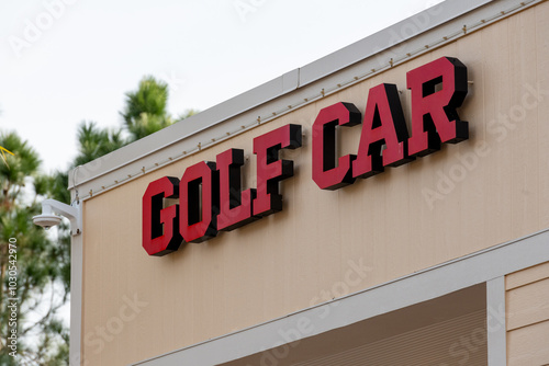 An electric channel letter sign or halo lit with bright red letters. The sign board and golf cart are attached to the exterior of a cream building with white trim. The business sign has black trim.