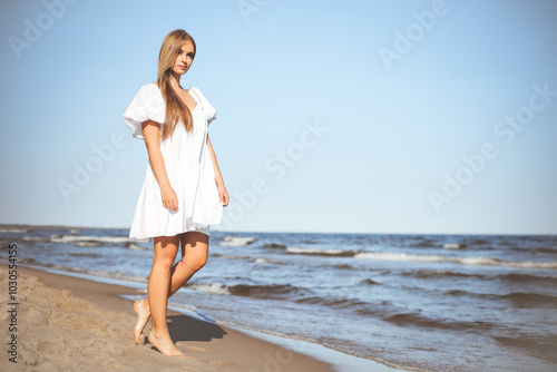 Happy smiling beautiful woman is walking on the ocean beach in a white summer dress