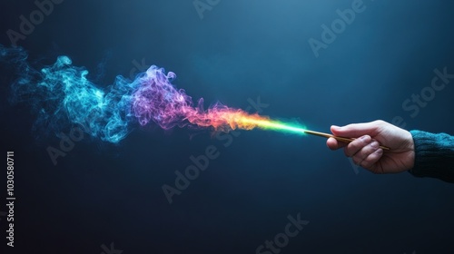Hand holding a magic wand with colorful smoke coming out of it, creating an artistic and mysterious atmosphere in a dark background.