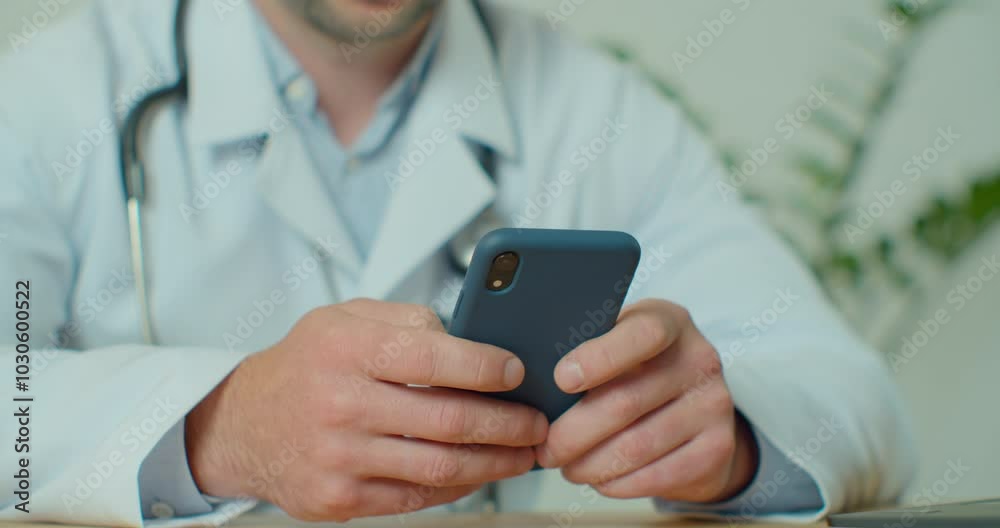 Male doctor in white coat using modern smartphone device with touch screen. Doctor using mobile phone texting to patient informing about medical test results.