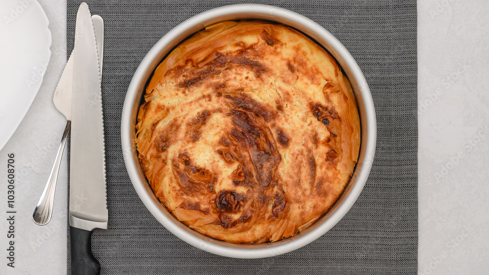Freshly baked phyllo dough pie with a golden crust close-up on a kitchen table, just out of the oven Freshly baked phyllo dough pie with a golden crust close-up on a kitchen table, just out of the oven