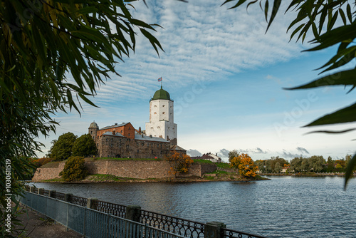 Vyborg Castle in Russia, standing on a small island surrounded by water, under a blue sky with clouds. This historic medieval fortress is a key tourist attraction in the Vyborg region.