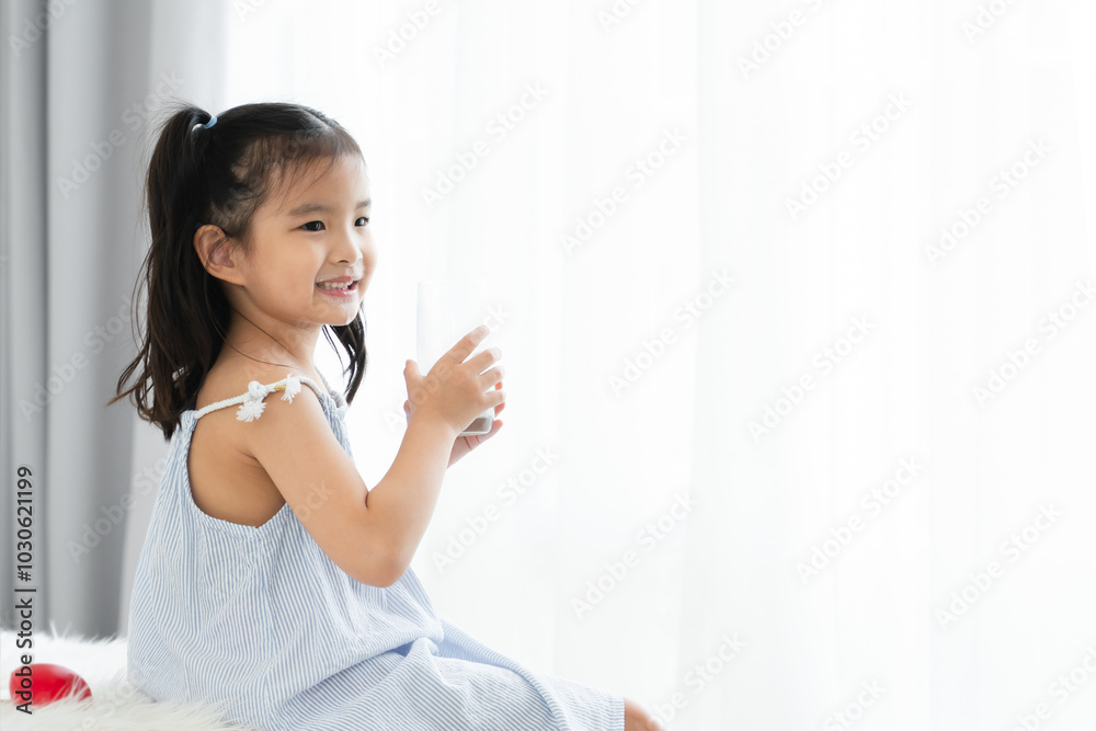 Asian little cute kid with mustache of milk on lips, holding a glass of milk, sitting at home. Young preschool child girl smiling, enjoy drinking milk for good health for breakfast in morning Asian little cute kid with mustache of milk on lips, holding a glass of milk, sitting at home. Young preschool child girl smiling, enjoy drinking milk for good health for breakfast in morning