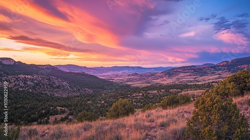 Vibrant sunset over rolling hills in a tranquil valley surrounded by mountain ranges in the late afternoon