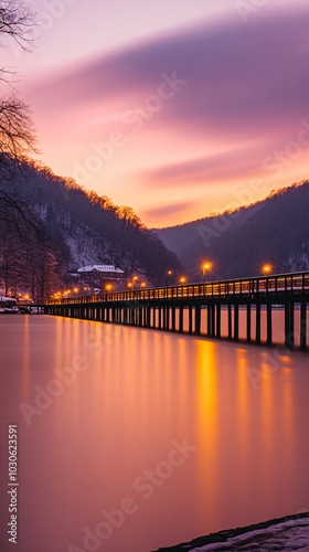 Wallpaper Mural A wooden bridge stretches across a calm lake at sunset, with a vibrant pink and purple sky above. The water reflects the warm glow of the lights on the bridge. Torontodigital.ca