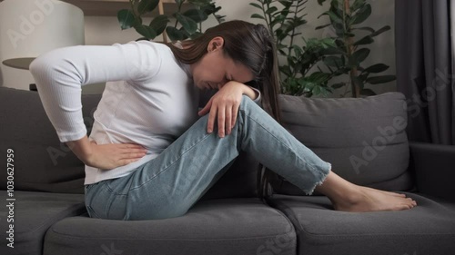 Flatulence young woman hand in stomach ache, suffer from food poisoning, abdominal pain and colon problem, gastritis or diarrhoea sitting on couch at home. Patient belly, abdomen or inflammation