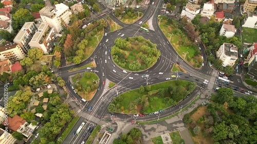 High angle drone footage of Herastrau and Piata aviatorilor Bucharest Romania. Green roundabout seen on a sunny day during golden hour. Traffic navigating a rotary intersection. Flowing traffic.
 photo