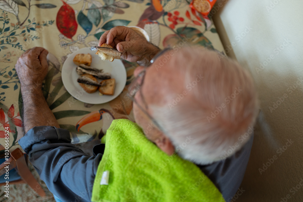 zenithal image of an eighty-year-old man having breakfast, eating toast with sardines and a cup of milk.