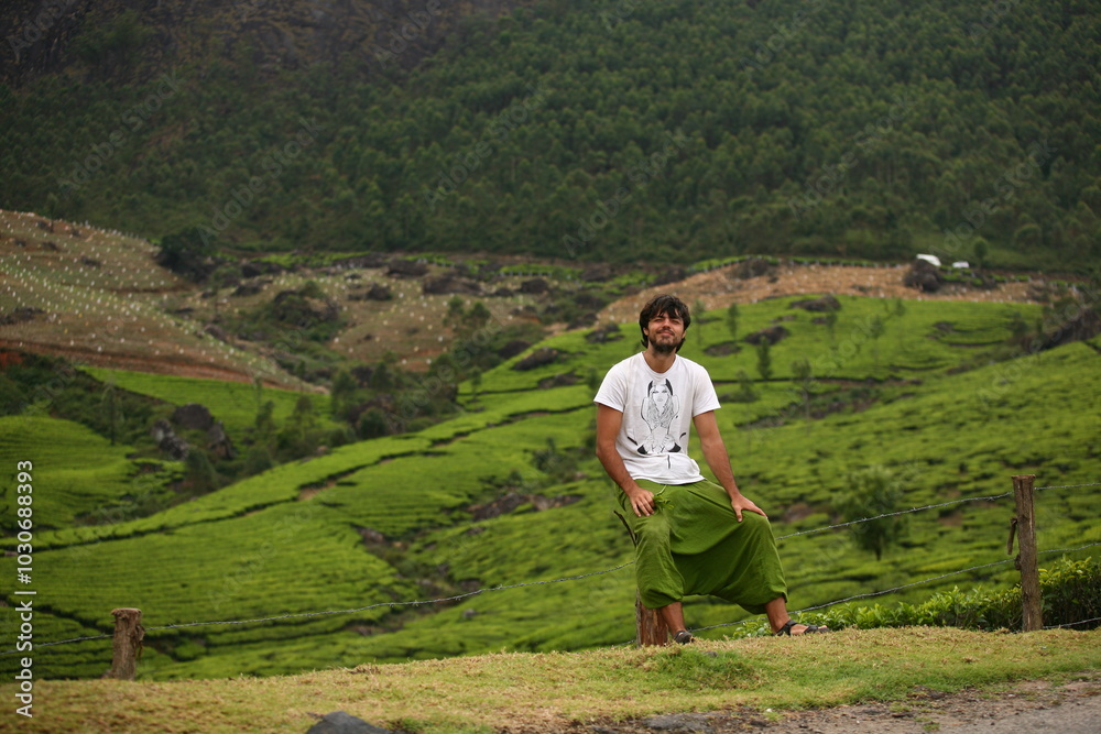 Happy smiling man solo traveller sitting in the mountains of Munnar, on tea plantations in India Happy smiling man solo traveller sitting in the mountains of Munnar, on tea plantations in India