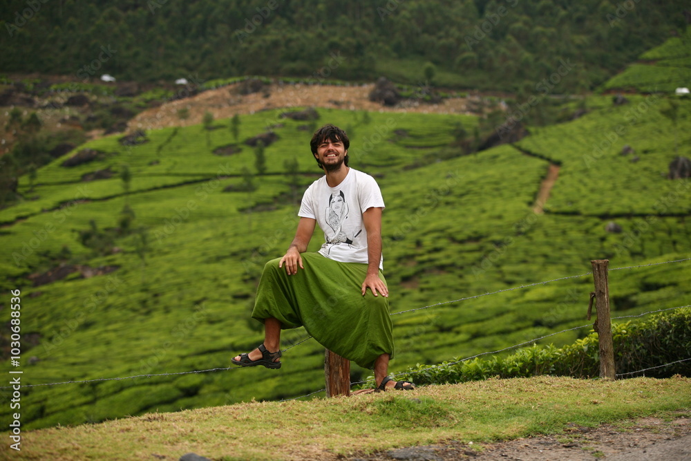 Happy smiling man solo traveller sitting in the mountains of Munnar, on tea plantations in India Happy smiling man solo traveller sitting in the mountains of Munnar, on tea plantations in India