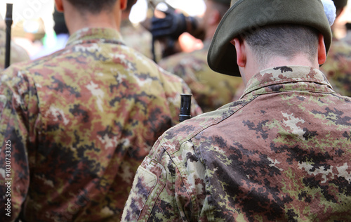 soldiers in camouflage uniforms seen from behind with hats during a parade