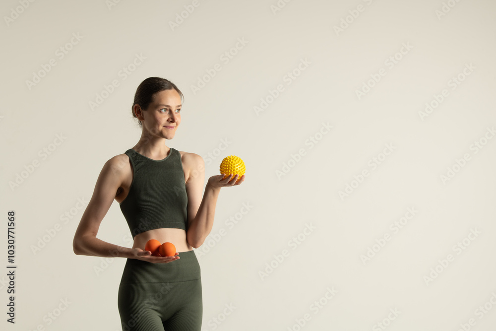 Smiling young woman or girl in green sportswear holding massage balls and looking away. Standing on a white background. Smiling young woman or girl in green sportswear holding massage balls and looking away. Standing on a white background.