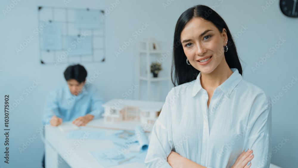 Closeup of female professional architect engineer cross arms with confident while skilled coworker focus on drawing blueprint at table with house model. Creative living and design concept. Immaculate. Closeup of female professional architect engineer cross arms with confident while skilled coworker focus on drawing blueprint at table with house model. Creative living and design concept. Immaculate.