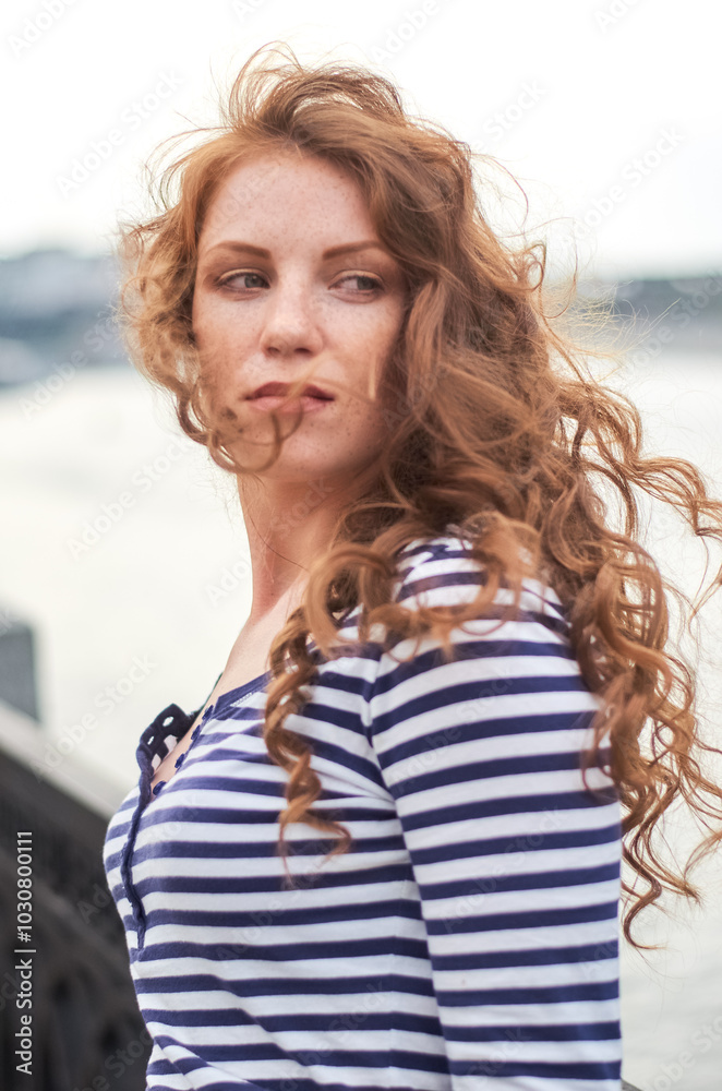 A woman in a striped shirt and white skirt stands on a pier against the backdrop of tall buildings. A woman in a striped shirt and white skirt stands on a pier against the backdrop of tall buildings.