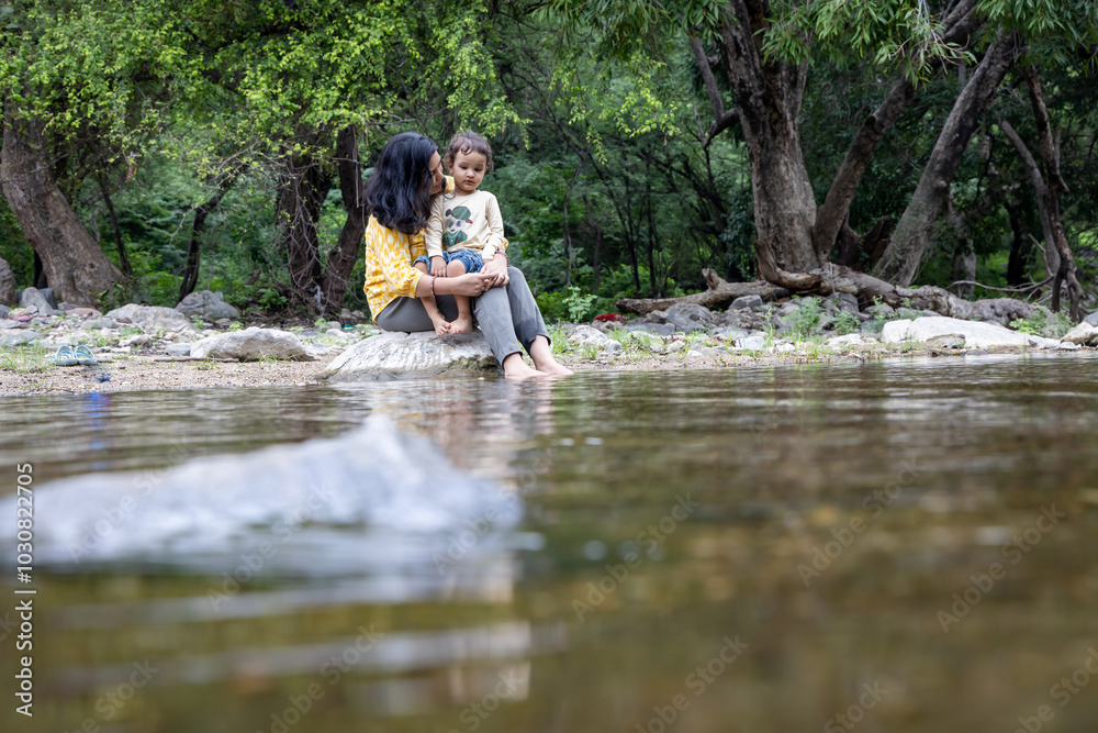 Fototapeta premium Isolated Woman Spending Quality Time with Son on Stone at Calm Lake Shore in the Morning